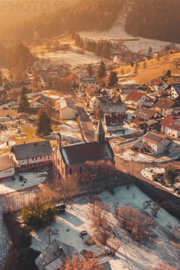 Snowy village with central church, warm sunlight bathes the surrounding area in golden tones, Enzklösterle, Calw district, Germany