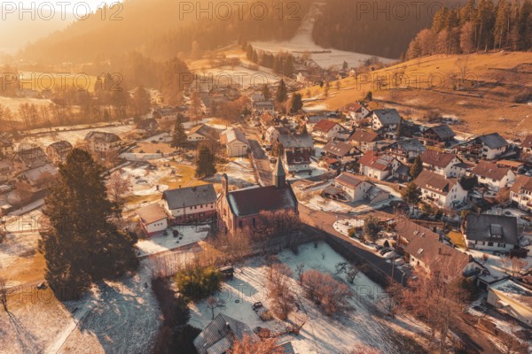 Snowy village with central church surrounded by snow-covered houses and warm golden light, Enzklösterle, Calw district, Germany