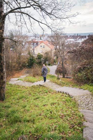 A woman walks down a stone staircase surrounded by trees and autumn leaves in an urban park, Herrenberg, Böblingen district, Germany