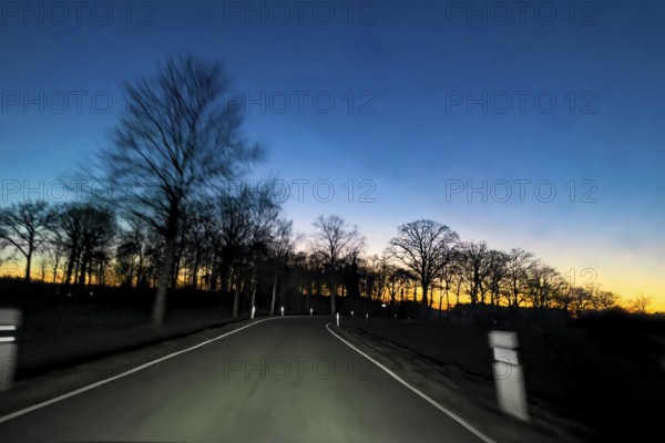 View from speeding speeding car at dusk at nightfall on a country road illuminated by headlights without a median strip with risk of game accident, Germany