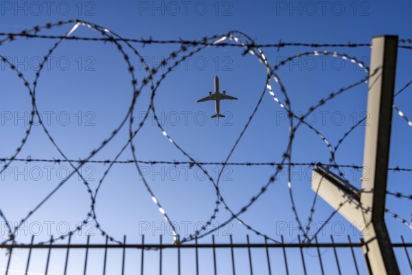 Symbolic picture security at the airport, outer fence at Düsseldorf International Airport, steel wire fence, with S-wire rollers, NATO wire, on the fence crown, airplane taking off, North Rhine-Westphalia, Germany