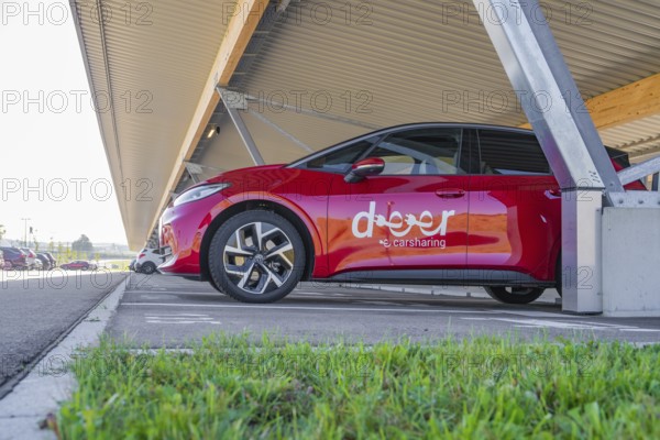 Red car sharing car under covered parking lot in sunny weather. Modern urban environment, ID3, Deer e-Carsharing, Germany