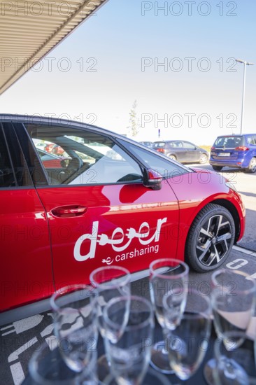 Red car sharing car in parking lot with glasses in the foreground, sunny weather and city atmosphere, ID3, Deer e-Carsharing, Germany
