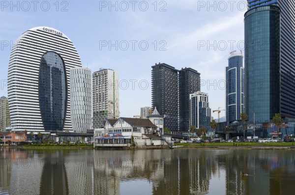 Modern high-rise buildings with glass facades are reflected in a calm lake under a cloudy sky, Batumi, Black Sea, Ajara region, Adjara, Autonomous Republic, Georgia