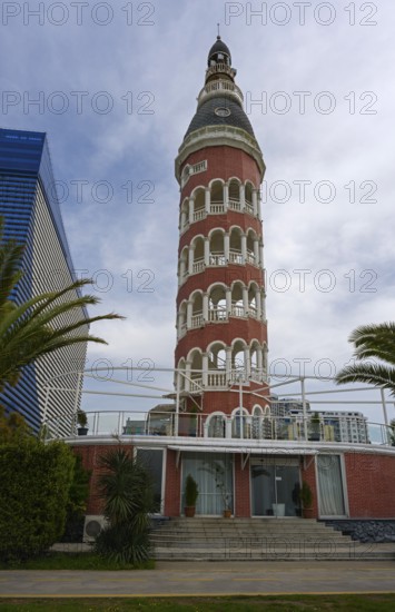A historic brick tower with round arches stands next to palm trees and modern architecture under a cloudy sky, Tower and Brewery Restaurant, Batumi, Black Sea, Ajara Region, Adjara, Autonomous Republic, Georgia