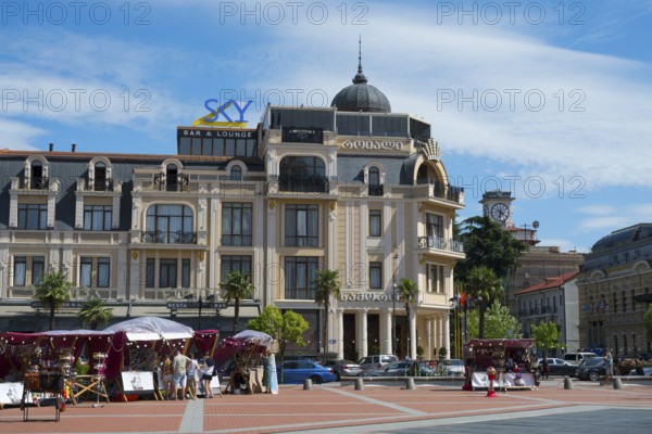 Market with stalls and people in front of a historic building with decorative roof, Royal Casino and Hotel, Europe Square, Batumi, Black Sea, Ajara region, Adjara, Autonomous Republic, Georgia