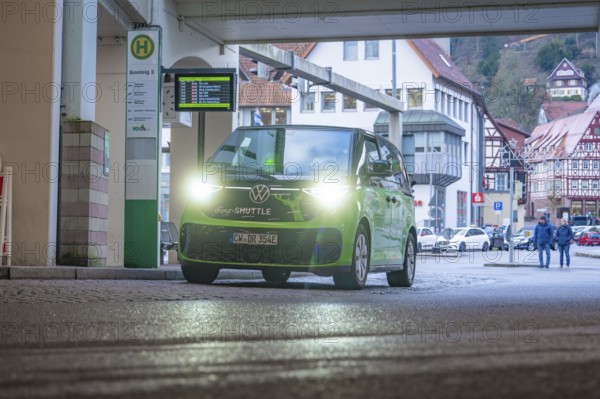 Green shuttle at a covered stop, surrounded by half-timbered houses, Deer E-Mobility Shuttle Service, Calw, Germany
