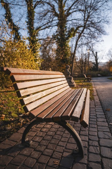 Empty park bench on cobblestone path surrounded by autumn trees, Stadtgarten Pforzheim, Germany