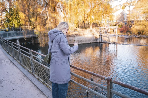 Woman photographing a river on an autumn day, Stadtgarten Pforzheim, Germany