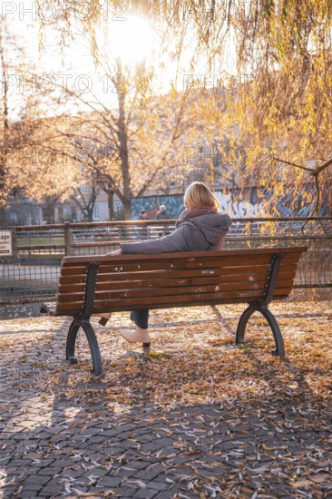 Woman sitting on park bench surrounded by autumn trees in sunlight, Stadtgarten Pforzheim, Germany