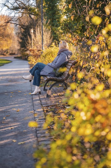 Woman sitting on park bench along an autumnal path, Stadtgarten Pforzheim, Germany