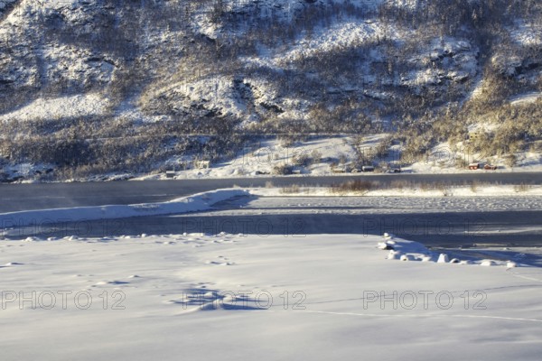 Snowy shore of a lake with hills and isolated houses, Norway