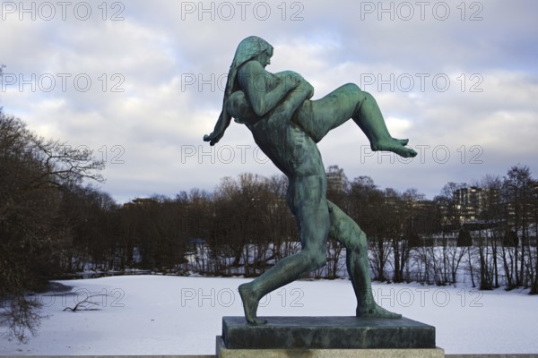 Bronze statue of a man carrying a woman. Winter landscape, icy river in the background, Vigeland sculpture park Oslo Norway