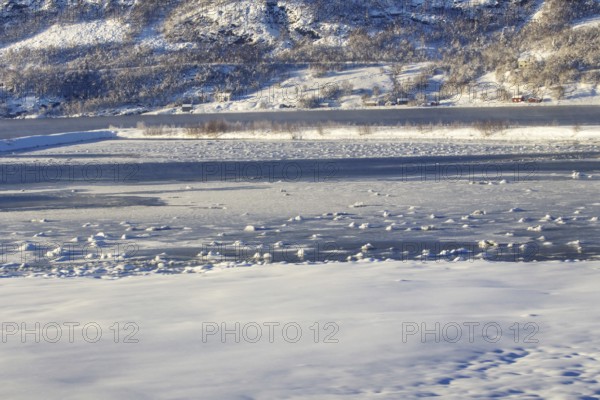 Frozen lake with snowy shore and hills in the background Norway