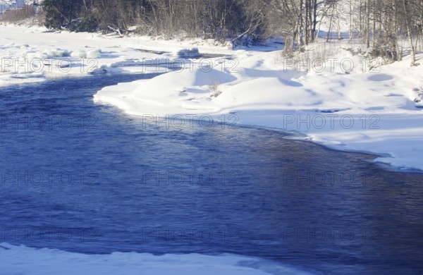 A river that flows through snow-covered landscape surrounded by trees in winter Norway