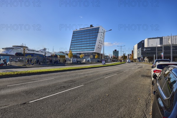 Schwedenkai ferry terminal, casino, general architecture, commercial building, modern architecture, lantern, lanes, central island, parking strip with cars, metal fence, ferry, trees, lawn, pedestrian as accessories, blue sky, cloudless, Kaistraße street, Kiel, state capital, district-free city, Schleswig-Holstein, Germany