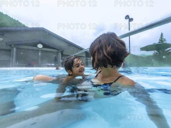 Mother and son are smiling while swimming in the miette hot springs located in jasper national park, alberta, canada, surrounded by steam and a mountain view
