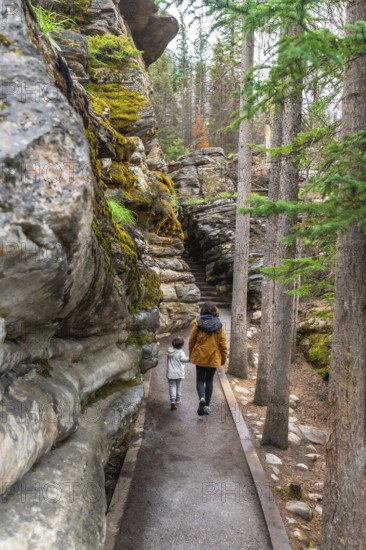 Mother and child enjoying a leisurely walk along a paved path, surrounded by lush green trees and moss covered rock formations at athabasca falls in jasper national park, alberta, canada