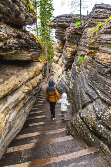 Mother and child walking down wooden stairs among layered sandstone cliffs at athabasca falls in jasper national park, a popular tourist destination in the canadian rockies