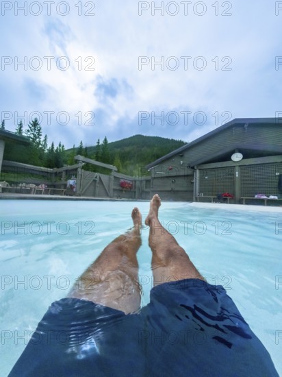 Tourist relaxing in the miette hot springs, surrounded by the breathtaking beauty of jasper national park, with legs extended in the turquoise water