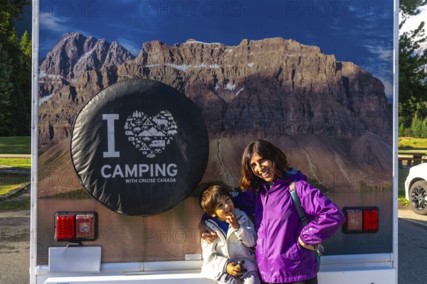 Mother and son posing happily in front of their rv, featuring a large i love camping graphic and a stunning view of mount robson in the canadian rockies
