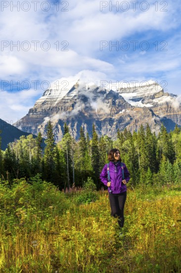 Female hiker walking through a meadow enjoying the view of mount robson on a sunny day with clouds and blue sky in mount robson provincial park, british columbia, canada
