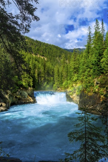 Turquoise fraser river flowing through lush green forest in mount robson provincial park, british columbia, with overlander falls cascading under a bright blue sky