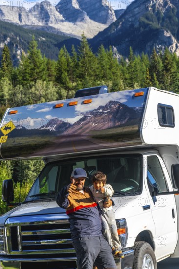 Father and son showing thumbs up, enjoying their rv trip in the majestic canadian rockies near mount robson, british columbia, with their camper van featuring a scenic mountain road decal