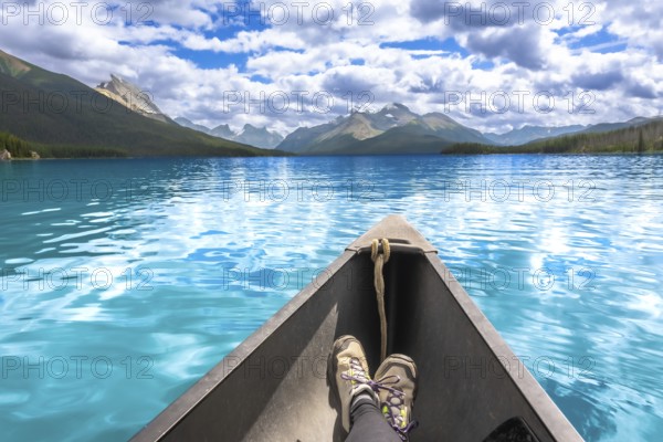 Turquoise maligne lake and surrounding mountains reflecting in the calm water with a person wearing hiking boots relaxing in a canoe in jasper national park, alberta, canada