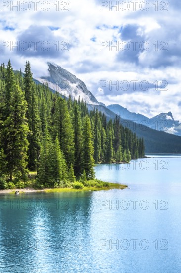 Turquoise maligne lake reflecting a cloudy sky, surrounded by lush pine forests and rocky mountains in jasper national park, a breathtaking unesco world heritage site