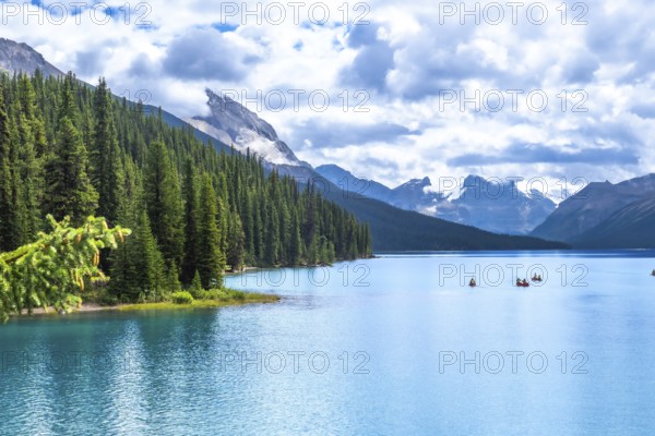 Tourists canoeing on turquoise maligne lake, surrounded by pine forests and snow capped mountains, create a breathtaking summer scene in jasper national park, alberta