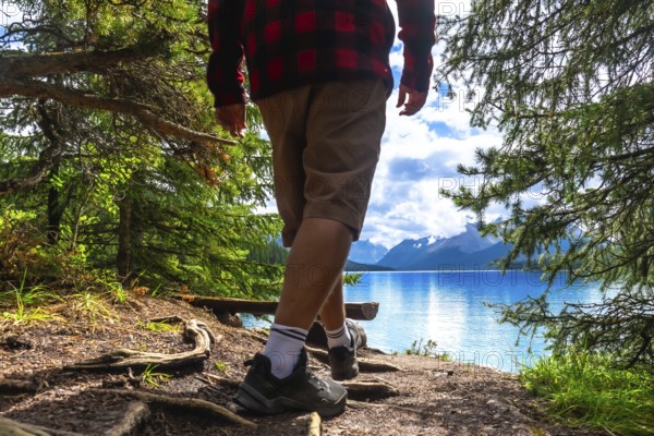 Hiker walking along a forest path toward maligne lake's turquoise waters, framed by a mountain range and a cloudy sky in jasper national park, alberta, canada