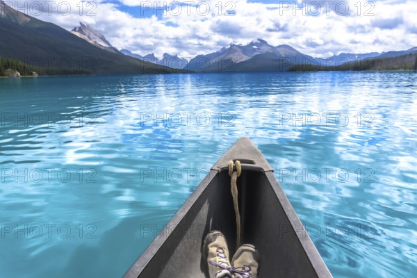 Hiking boots inside a canoe navigating the turquoise waters of maligne lake with its surrounding mountains and forests in jasper national park in the canadian rockies, alberta, canada