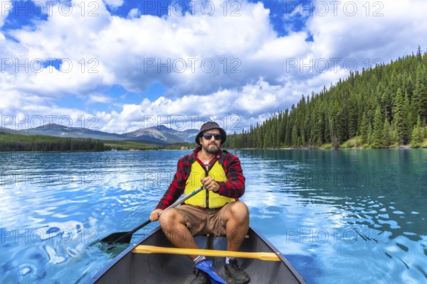 Tourist paddling a canoe on turquoise maligne lake with spirit island in the distance, enjoying the breathtaking scenery of jasper national park in the canadian rockies