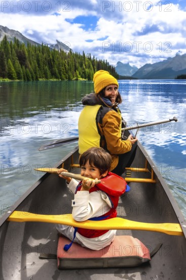 Mother and son paddling a canoe on maligne lake's turquoise waters, surrounded by mountains and pine trees in jasper national park on a sunny summer day