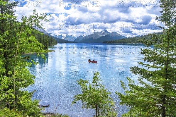 Two tourists enjoying a canoe ride on the turquoise waters of maligne lake, surrounded by lush trees and the majestic canadian rockies in jasper national park