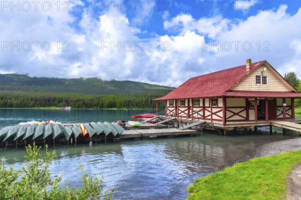 Colorful canoes and kayaks resting on a wooden dock in front of a boathouse on the beautiful maligne lake in jasper national park, with the canadian rockies in the background under a summer sky