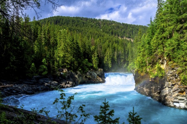 Flowing turquoise water of the fraser river winds through a lush green forest toward overlander falls in mount robson provincial park, british columbia, under a cloudy sky