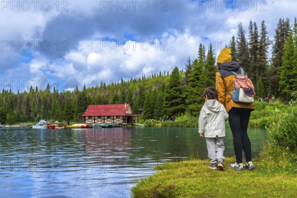 Mother and son enjoying the stunning view of the iconic boathouse on maligne lake, surrounded by the pristine nature of jasper national park on a sunny summer day