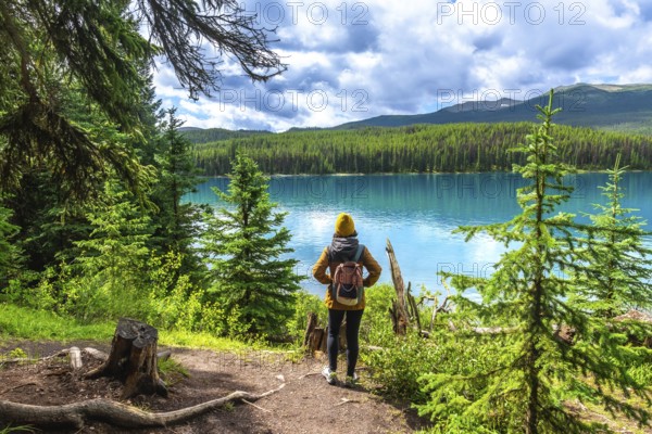 Female hiker with a backpack admiring the stunning turquoise waters of maligne lake, surrounded by lush evergreens and majestic mountains in jasper national park