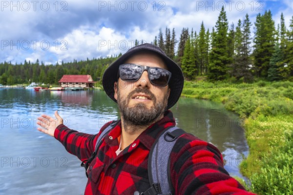 Happy tourist showing with open arms the beautiful maligne lake with the boathouse at jasper national park during a sunny summer day in alberta canada