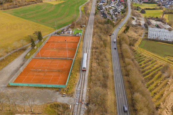 Aerial view of a landscape with railway tracks, tennis courts and roads, surrounded by fields and houses, historic event, first test run with a passenger train on the Hermann tracks, Hesse Railway since 1988, Ostelsheim, Calw district, Germany