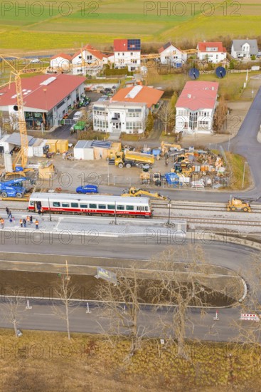A train passes a construction site with numerous buildings and a crane in a rural area, historic event, first test run with a passenger train on the Hermann tracks, Hesse Railway since 1988, Calw district, Germany