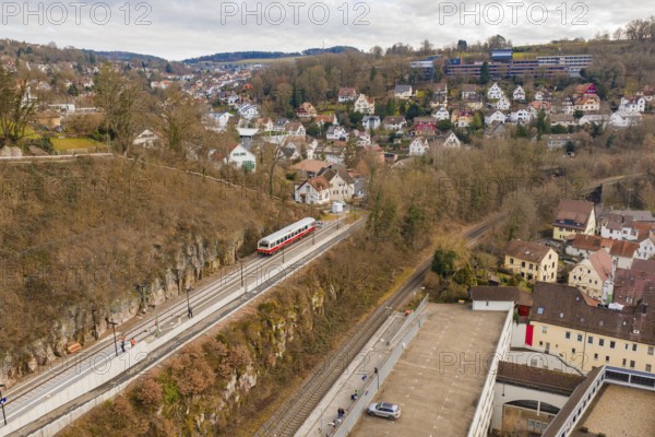 A train travels through a hilly area with urban houses and winter trees under a cloudy sky, historical event, first test run with a passenger train on the Hermann tracks, Hesse Railway since 1988, Calw, Calw district, Germany
