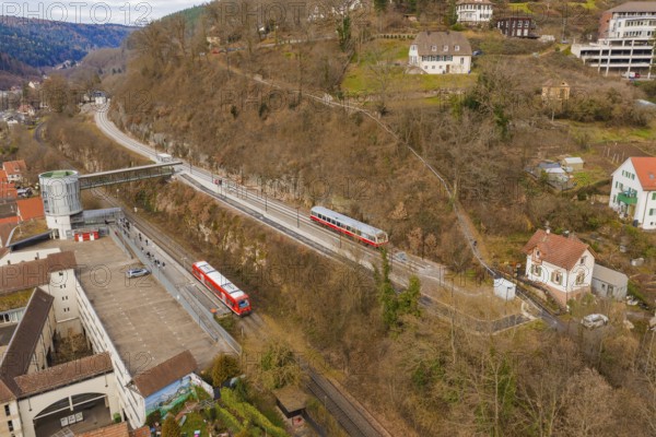 Two trains travel through an urban area with hills and buildings, surrounded by winter vegetation, historic event, first test run with a passenger train on the Hermann tracks, Hesse Railway since 1988, Calw, Calw district, Germany