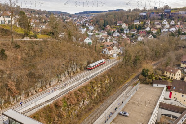 A train moves through an urban environment with hills and houses, surrounded by winter vegetation and clouds, historic event, first test run with a passenger train on the Hermann tracks, Hesse Railway since 1988, Calw, Calw district, Germany
