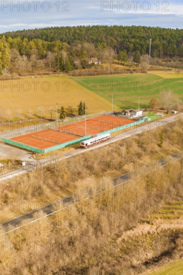 Land view of tennis courts next to a moving track, historic event, first test run with a passenger train on the Hermann tracks, Hesse railway since 1988, Ostelsheim, Calw district, Germany