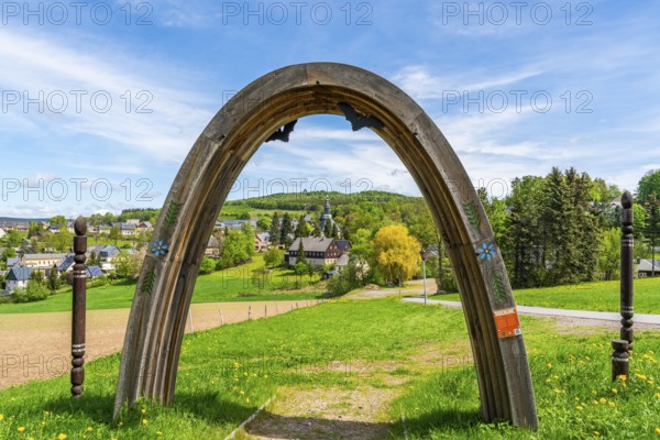 View through a wooden arch of residential buildings and landmarks of the historic mountain church, in the back forest on Schwartenberg, health resort and toy village Seiffen, Ore Mountains, Saxony, Germany