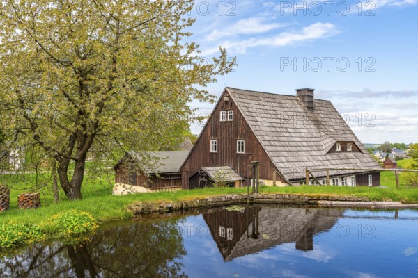 Historic houses with half-timbered timber and shingles on a pond under trees in the Seiffen open-air museum, Ore Mountains, Saxony, Germany