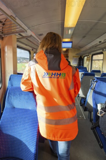 Person wearing safety clothing in the passenger area of a train, blue seat cover and looking outside, historic event, first test drive with a passenger train on the Hermann tracks, Hesse Railway since 1988, Calw district, Germany